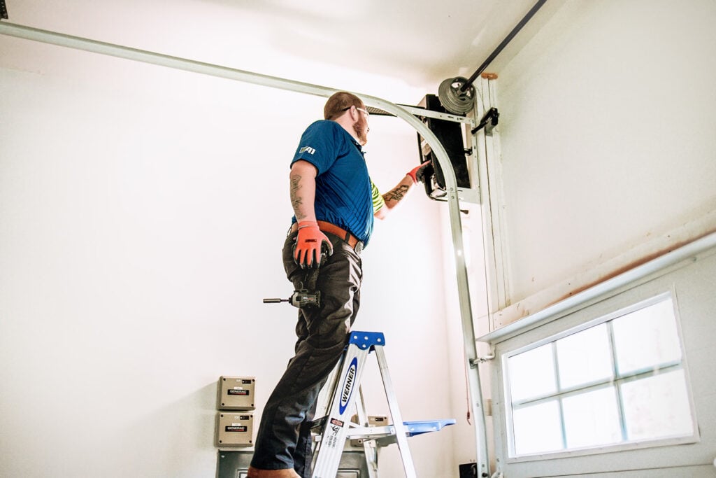 Technician performing maintenance on garage door with ladder